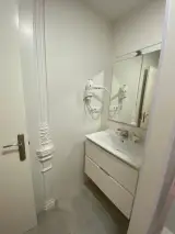 Vista del lavabo del baño desde la puerta, con mueble blanco de dos cajones y columna decorativa al lado